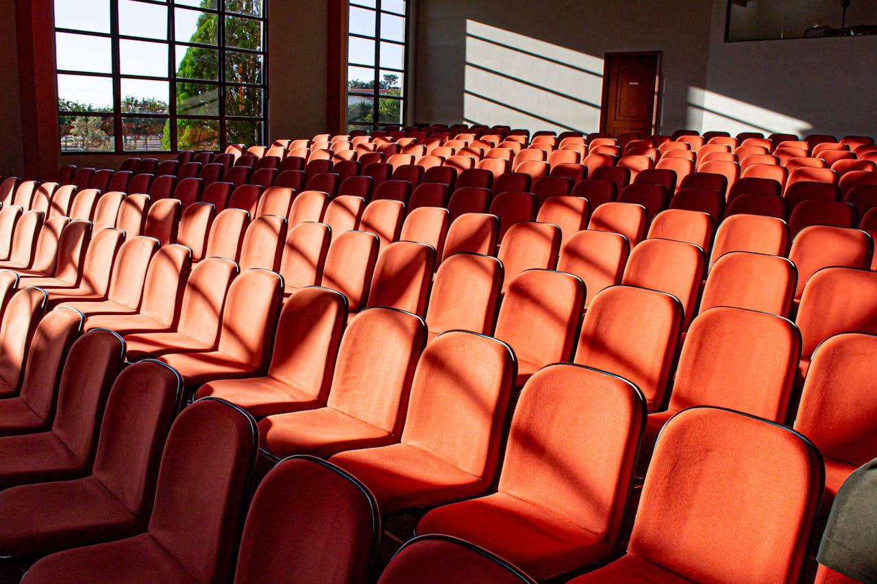 A sunlit, empty auditorium displaying rows of red chairs and shadow patterns.